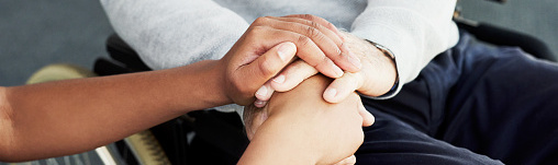Cropped shot of a nurse and an elderly patient in a wheelchair holding hands